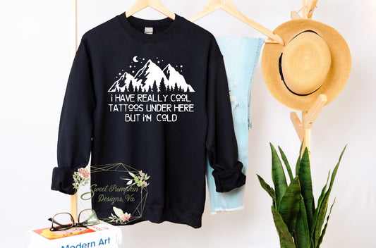 A trendy crewneck sweatshirt with a humorous graphic that reads 'I have really cool tattoos under here but I'm cold'. The graphic features bold typography. The sweatshirt is made from a soft and comfortable cotton blend and features ribbed cuffs and hem. It has a regular fit and a