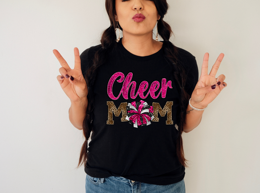 Leopard Print Cheer Mama Shirt featuring a bold design with a leopard print pattern, megaphone, pom poms, and the words 'Cheer Mama.' A stylish and trendy shirt for cheer moms to show their support. Perfect for competition cheer or everyday wear.