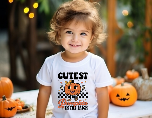 An adorable Halloween shirt for girls with the phrase 'Cutest Pumpkin In The Patch', featuring a preppy and playful design. The shirt adds a unique touch to her Halloween outfit, embodying the essence of cute Halloween fun.