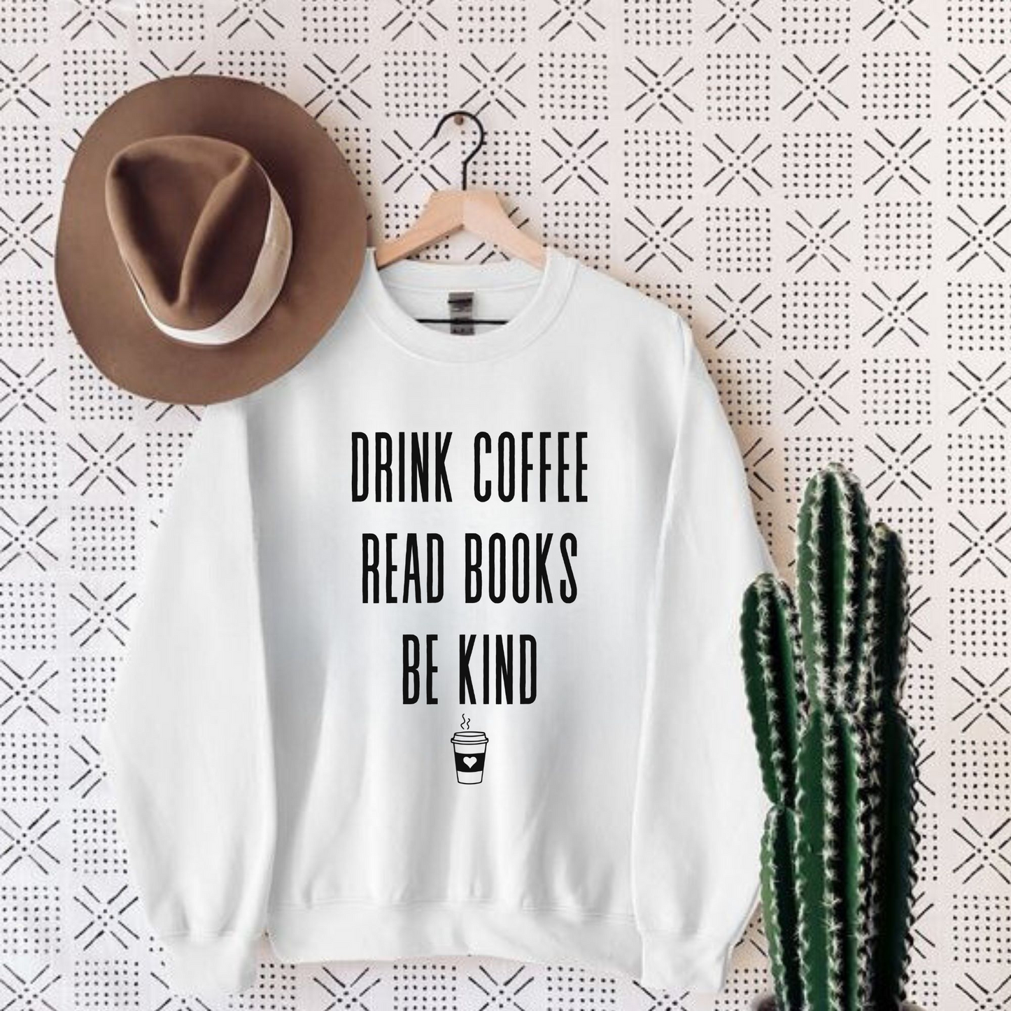 An oversized book lovers sweatshirt with the phrase "Drink Coffee, Read Books, Be Kind" written in bold letters. Perfect for book enthusiasts and lovers of literature.