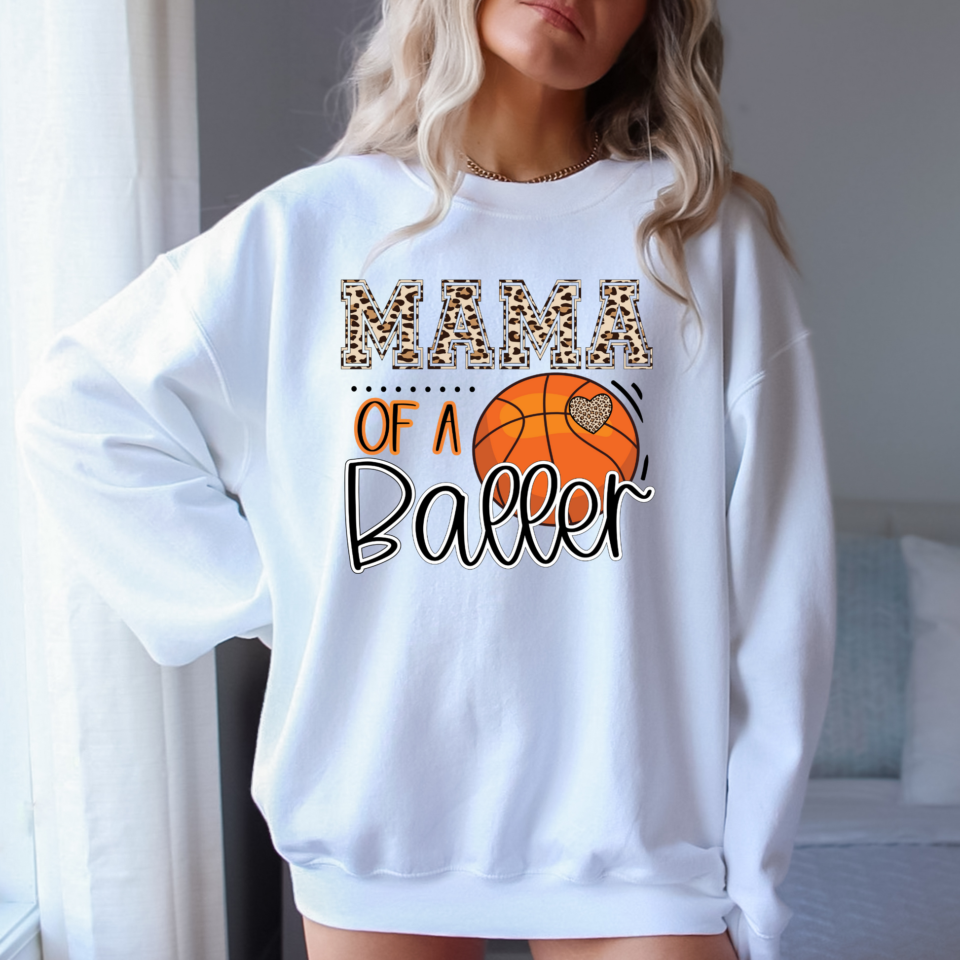 A cozy crewneck sweatshirt for basketball moms with the text 'Mama of a Baller'. This sweatshirt is perfect for game day, offering comfort and style for basketball moms supporting their players