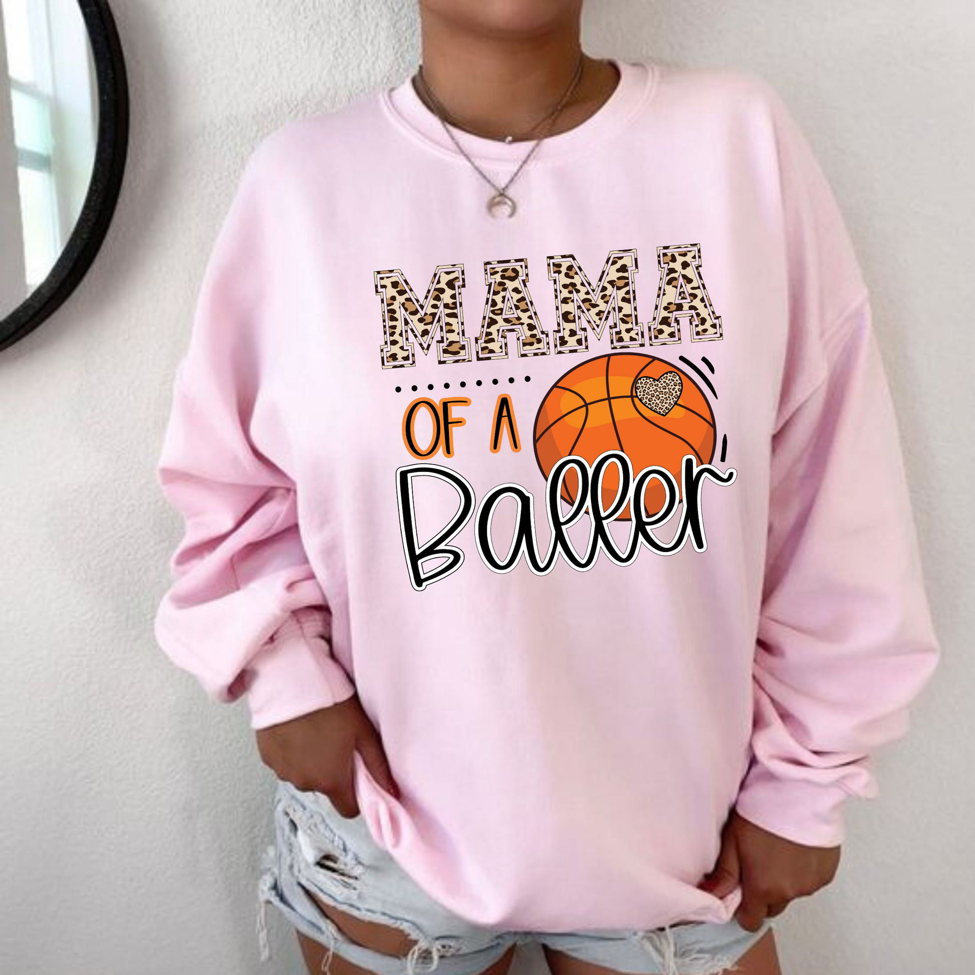 A cozy crewneck sweatshirt for basketball moms with the text 'Mama of a Baller'. This sweatshirt is perfect for game day, offering comfort and style for basketball moms supporting their players.