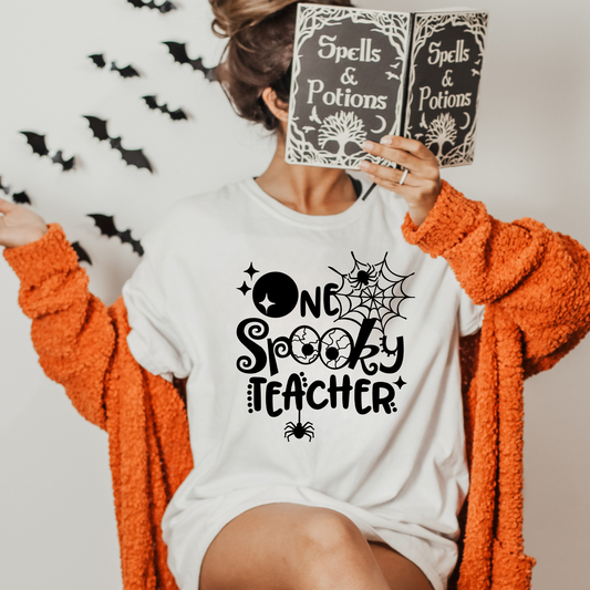 A cozy 'One Spooky Teacher' Halloween shirt, perfect for teachers looking to embrace the autumn spirit. The shirt features a playful design that adds a touch of Halloween charm to your fall outfit. Ideal for showcasing your teacher style with a dash of spooky fun.