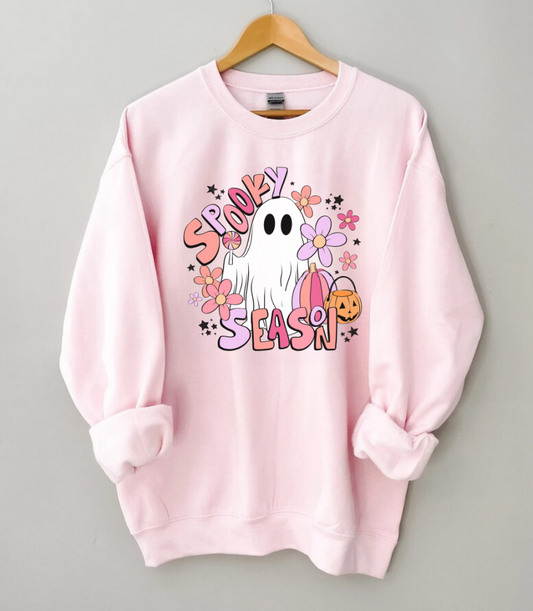 A trendy and oversized Halloween sweatshirt in pink, featuring a cute ghost design with the text 'Spooky Season'. This pastel pink fall sweatshirt adds a playful touch to your autumn wardrobe.