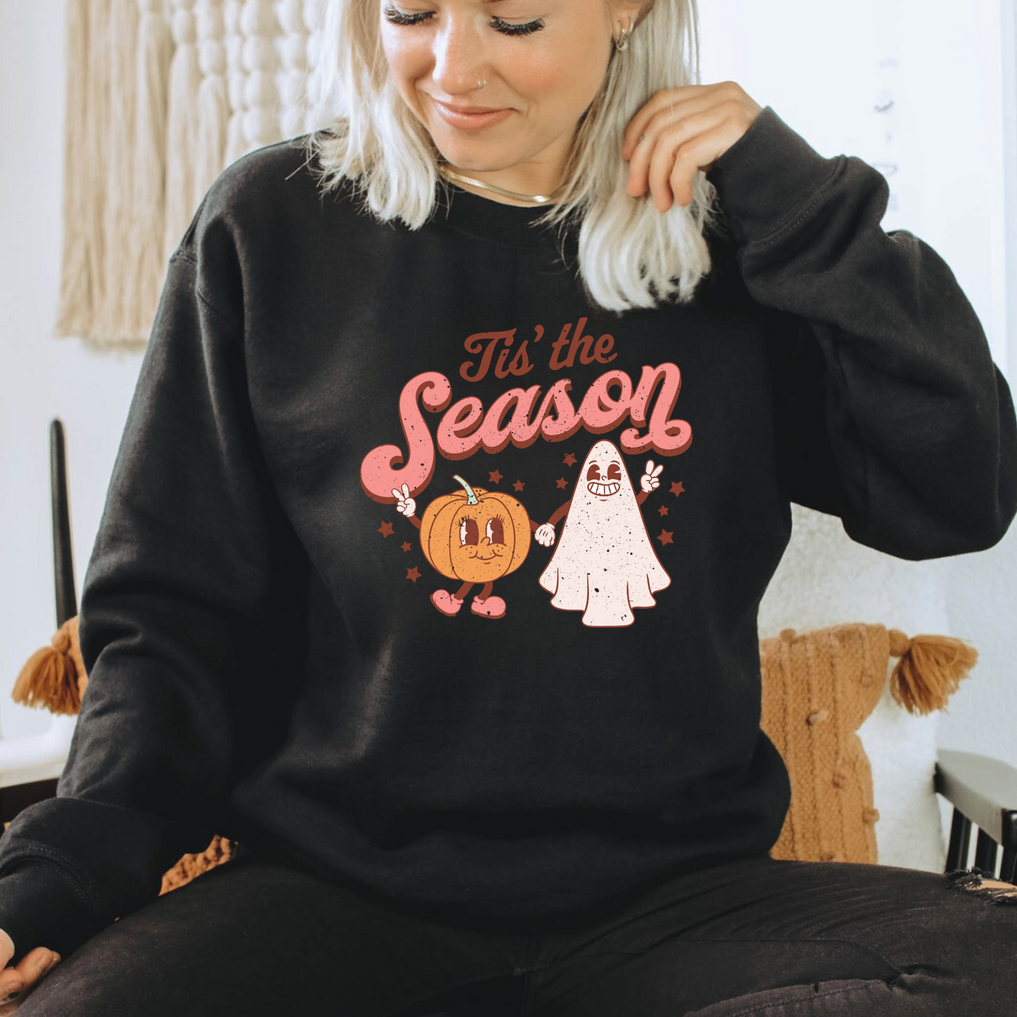 A retro, vintage Halloween sweatshirt crewneck with a cute ghost and pumpkin design. The sweatshirt features the slogan "Tis the Season" in bold, playful letters. The muted colors and vintage design add to the overall spooky aesthetic of the sweatshirt.